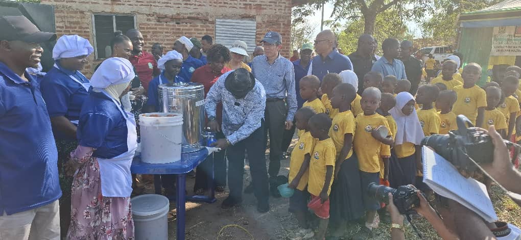 Hon Adam Malima , Commissioner of Morogoro region, serves soya milk  to pupils of of Hihud primary school during the official commissioning  of soya milk production project in Tanzania , looking at Prof. Li Xiaoyun, lead chair of CAU and prof. Xu Jin a fellow expert 