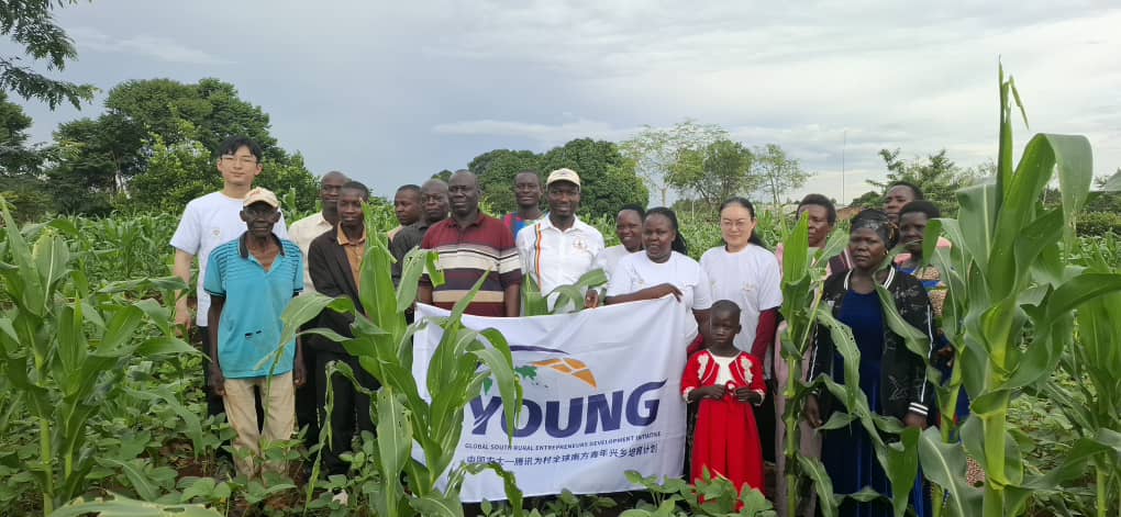 A photo moment of Dr. Li Li, Dr. Mula Anthony, Headteacher Makubo Stephen, and local farmers at the Buteme Light SDA Model School Garden in Busana Village, Kamuli District.
