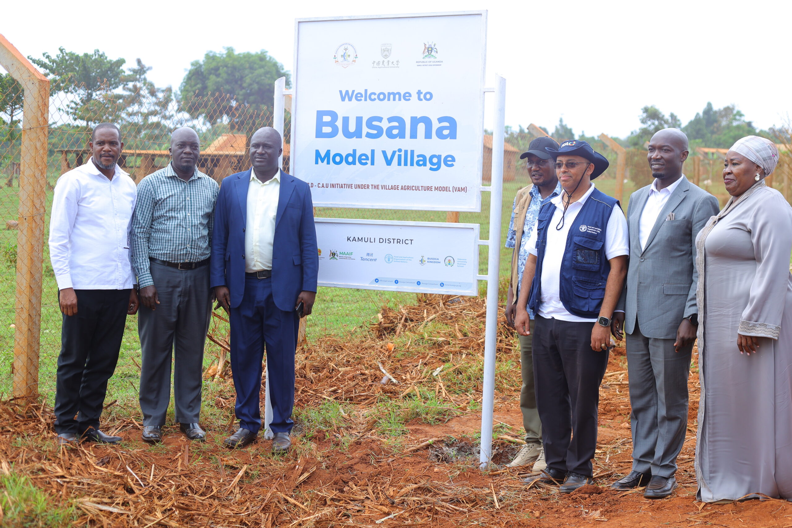 H.E. Ezana Getahun Kassa, FAO Country Representative in Uganda (third from right), is joined by Owek. Nasabu Nantale, Minister of Education of the Busoga Kingdom (far right); Mr. Isabirye Shabiru Kalulu, Vice Governor of the Busoga Consortium for Development (next to H.E. Kassa); Dr. Mula Anthony, Director General of the Busoga Consortium for Development (BCD); Hon. Stephen Kisa Bakubalwayo, Chairperson of the Busoga Parliamentary Caucus; HRH Isabalangira Samuel Zirabamuzale Nkuutu of Busoga; Mr. Dhizaala Kaloli of Kamuli District; and other leaders for a group photo at the Busana Model Village signpost during the FAO Representative's official monitoring visit to Kamuli District.